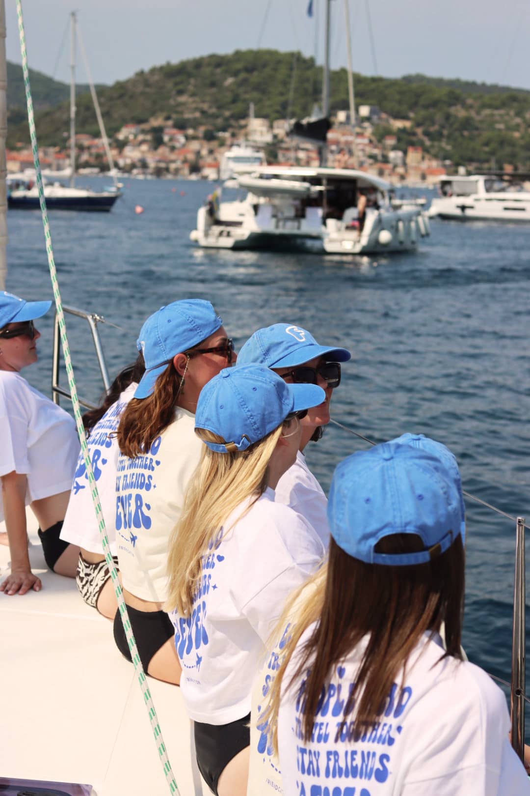 Tjejer med blå kepsar tittar ut över vattnet från kanten på en segelbåt.