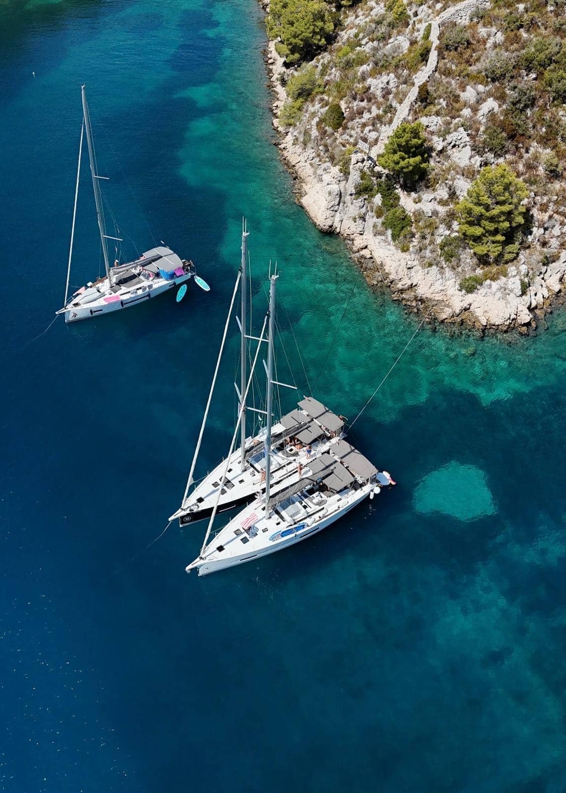 Segelbåtar ligger ankrade intill land i en turkos vik.