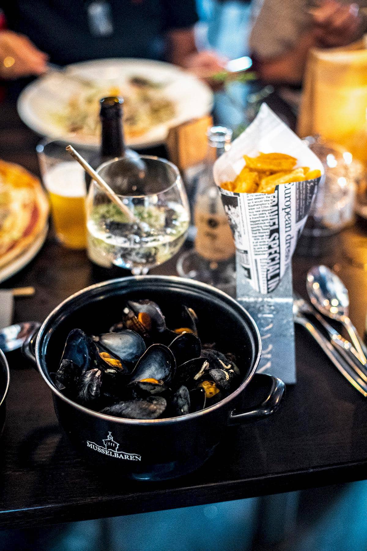 Ein Topf mit gekochten Miesmuscheln, dazu Pommes frites und Getränk.