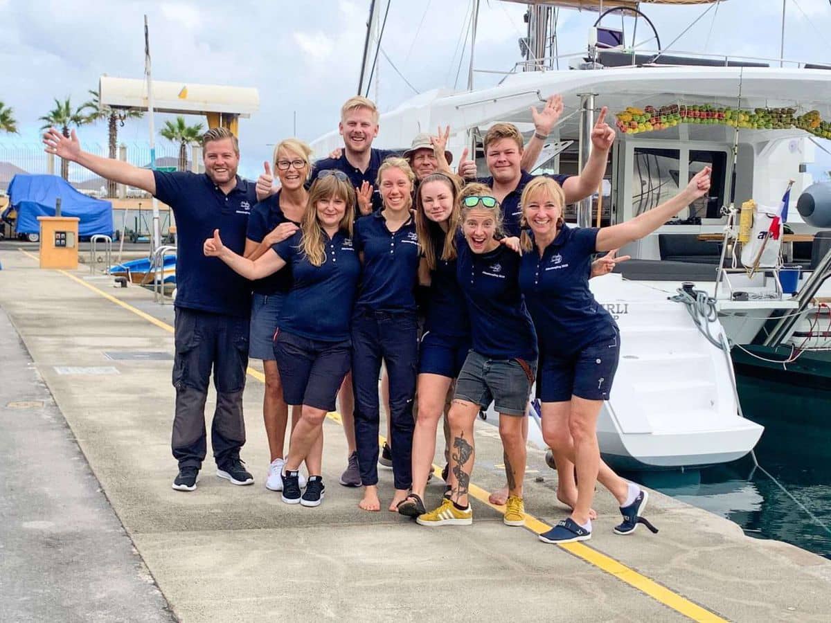 Gruppe af glade mennesker, der står foran en sejlbåd.