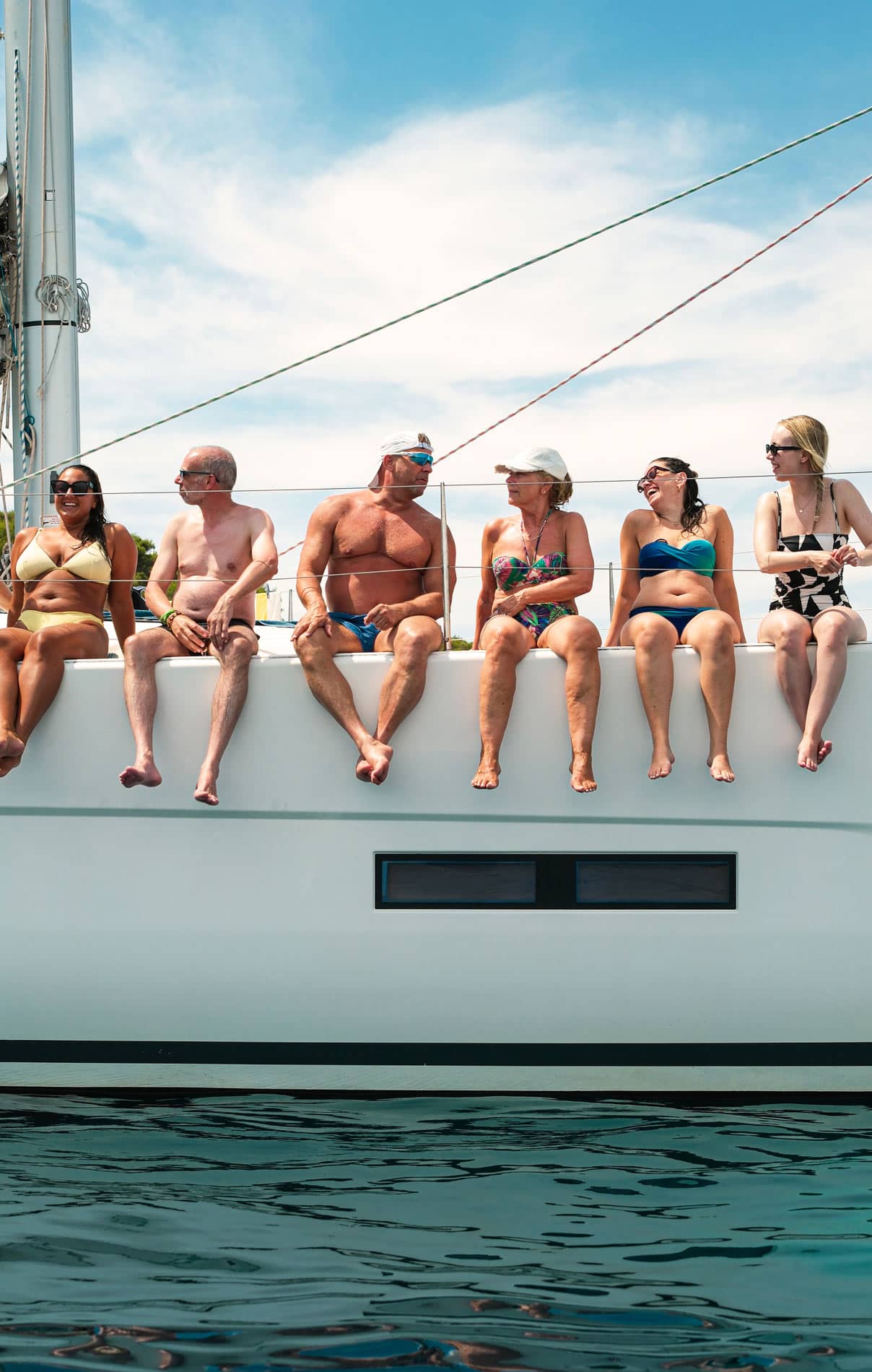 Sechs Gäste in Badekleidung sitzen an der Reling und lassen die Beine baumeln
