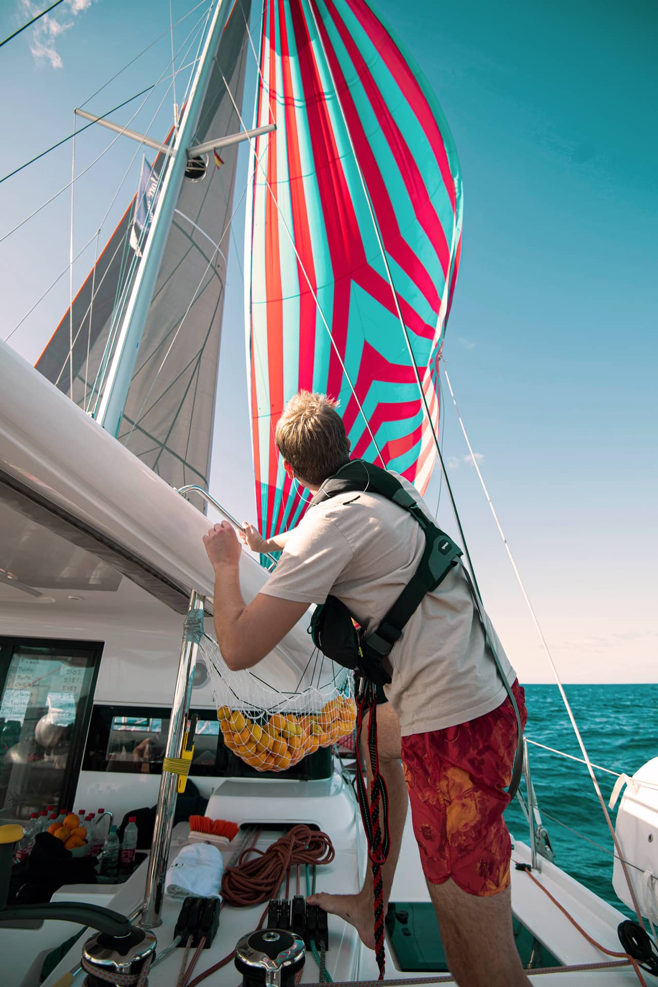 Ein junger Mann blickt auf das farbenfrohe Genua-Segel. Es ist rot und blau gemustert.