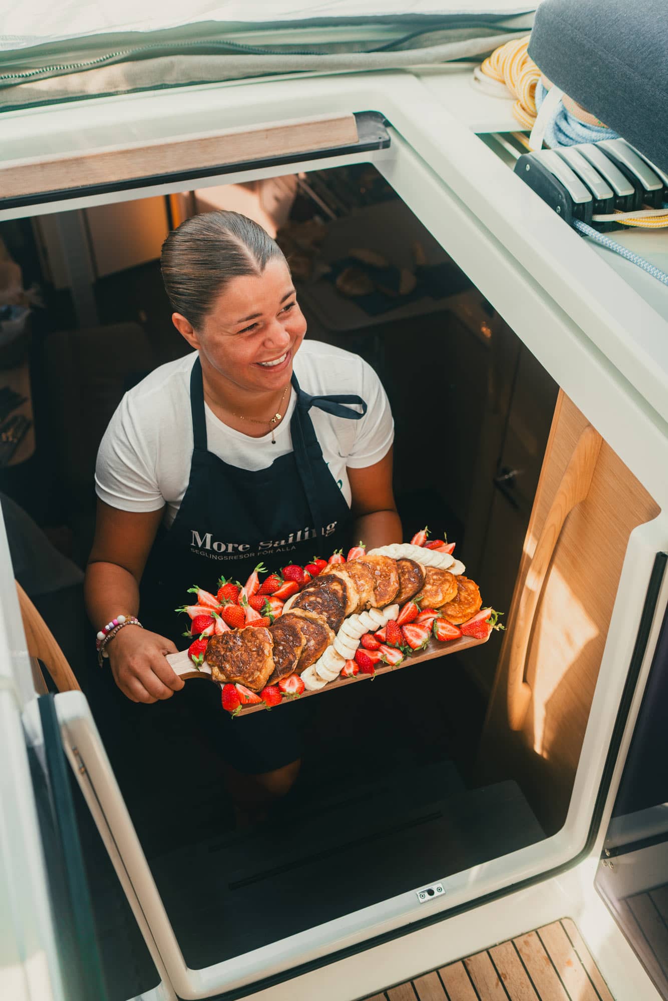 Värd kommer upp från segelbåten med en bricka med pannkakor, banan och jordgubbar.
