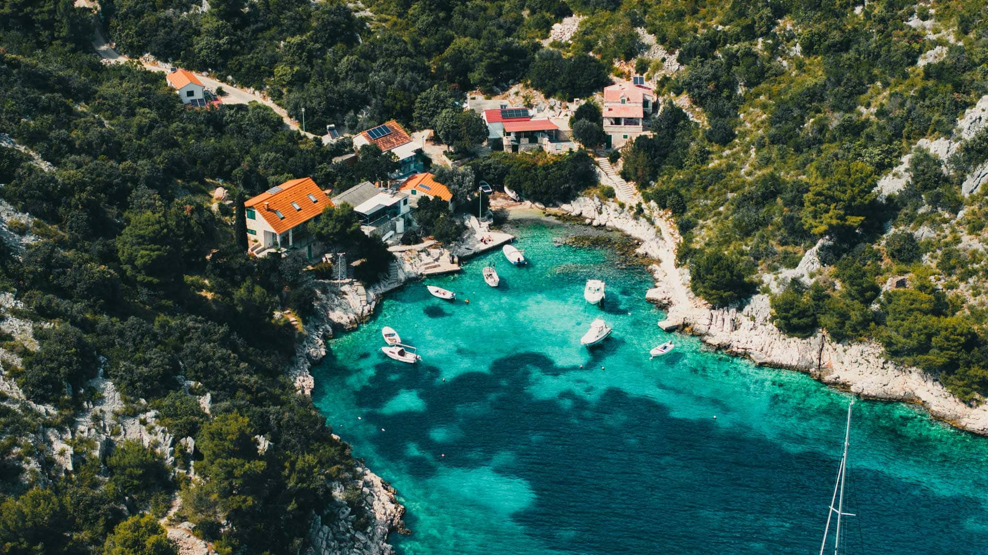 Bugt i Kroatien med små motorbåde og fem huse beliggende på klippekanten