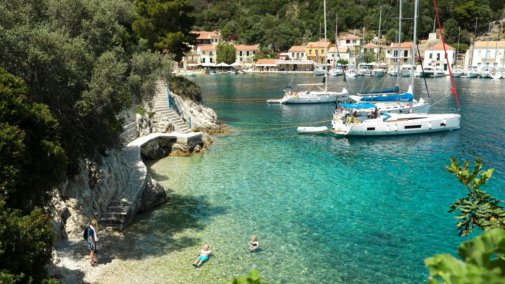 Bugt i Grækenland med turkisblåt vand og sejlbåde i det fjerne.