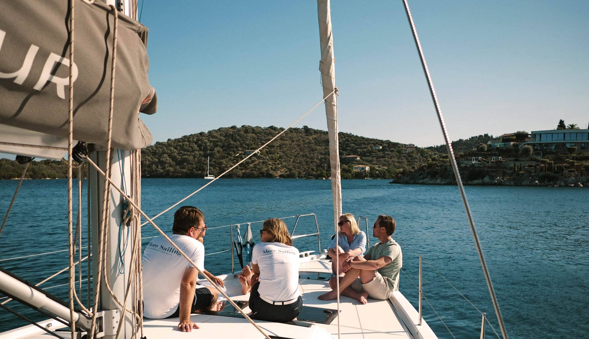 En Dufour 530 der ligger for anker ved en bugt, en gruppe mennesker sidder foran på båden