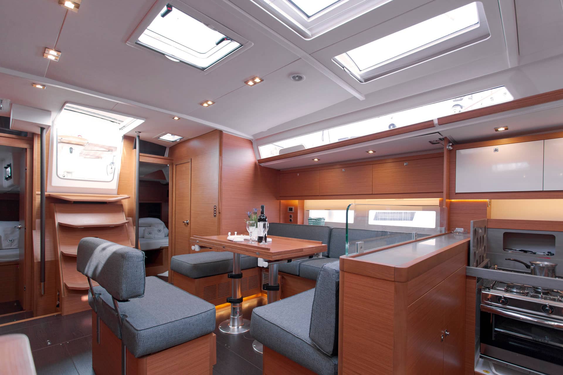 The saloon of a Dufour 530 with a wooden interior and a sofa with grey cushions
