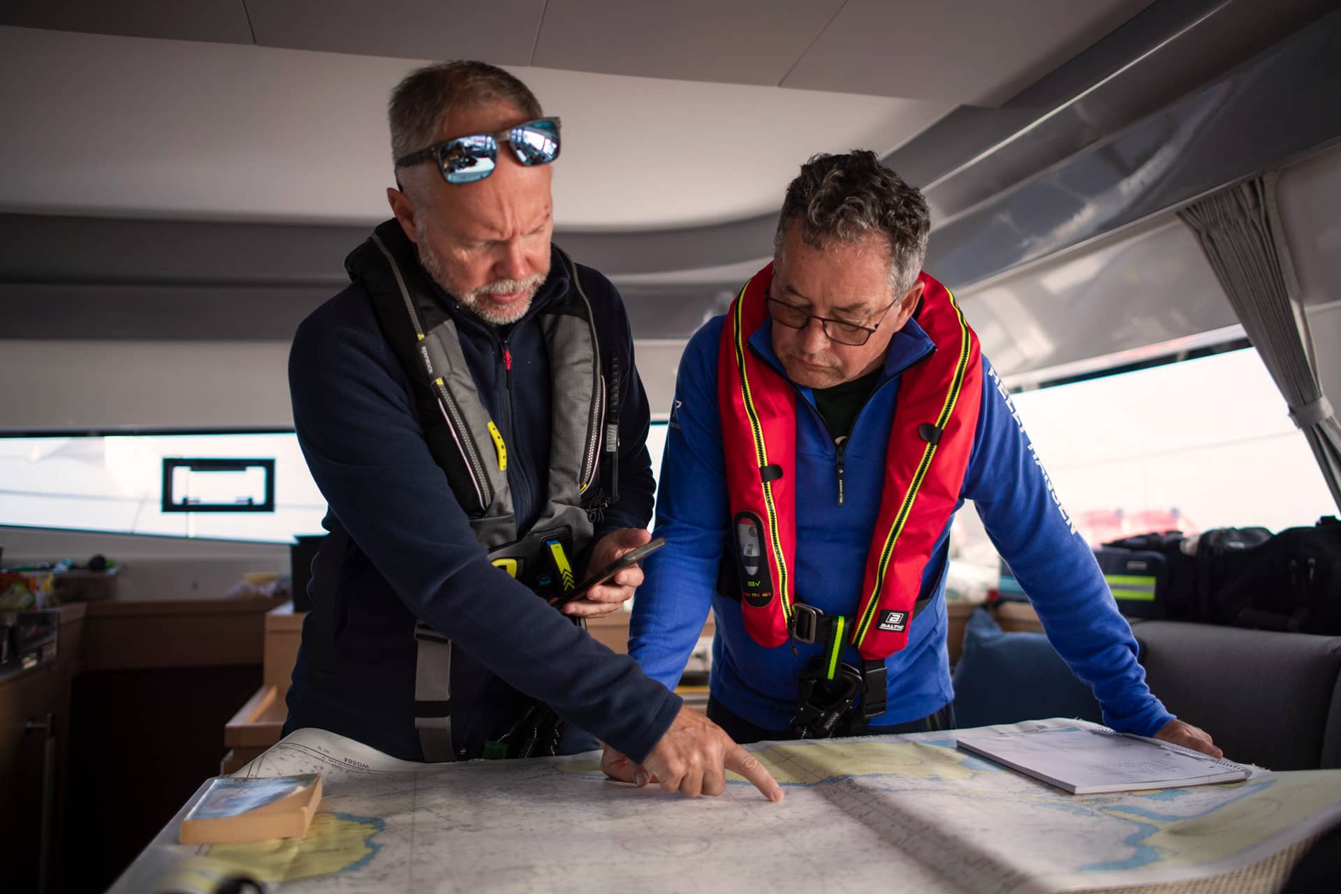 Zwei Männer in Schwimmwesten betrachten eine Seekarte und planen eine Route