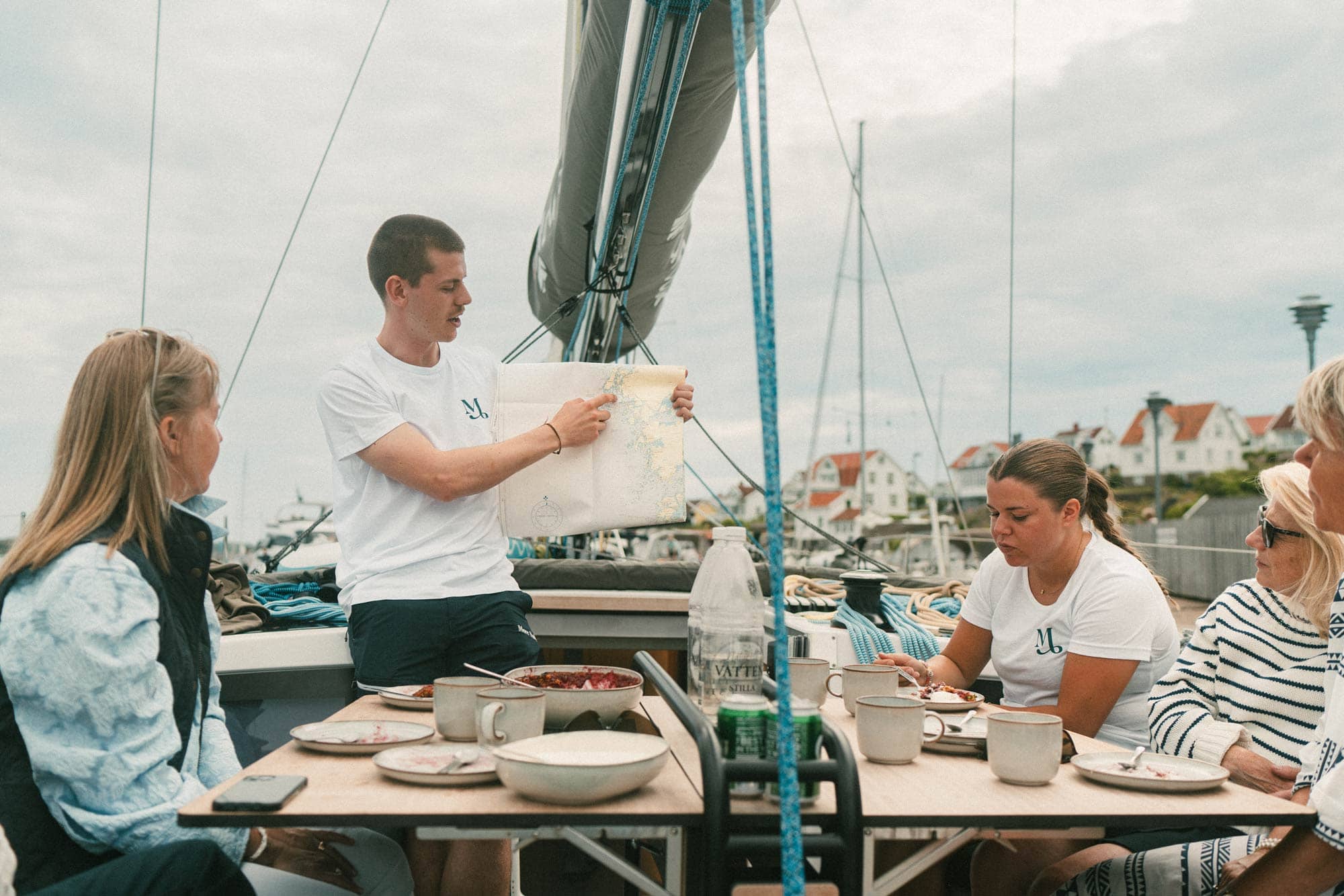 En skeppare visar på en karta vilken rutt båten ska ta. Gäster tittar på.