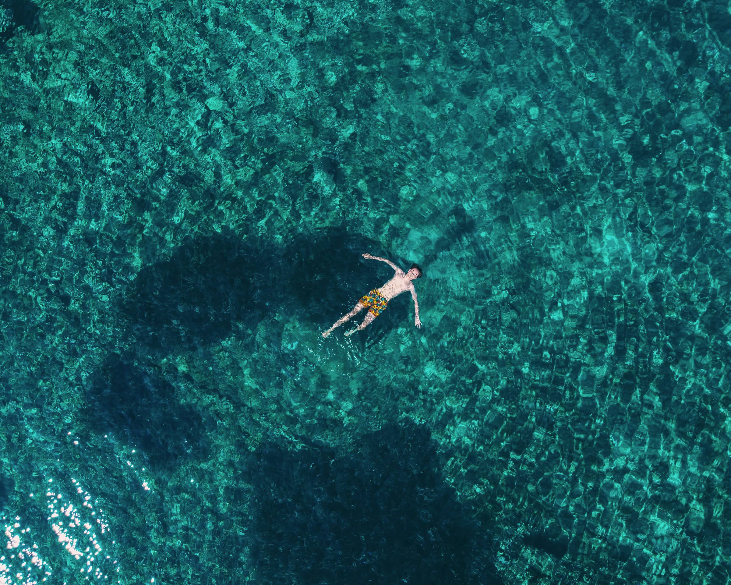 Mann schwimmt im türkisfarbenen Wasser auf dem Rücken. 
