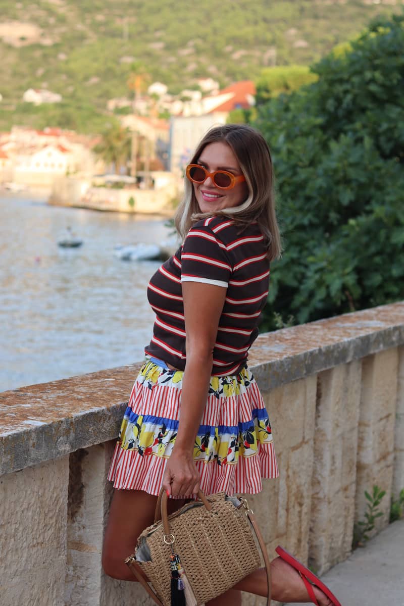 Tjej som är uppklädd i kjol, solglasögon och väska i hand.