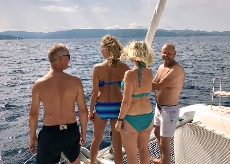 Fire voksne står i stævnen på en sejlbåd og kigger ud over havet.