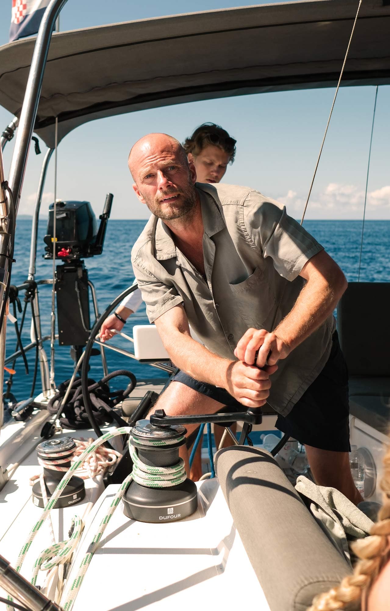 A male guest helps the skipper to winch and set sail