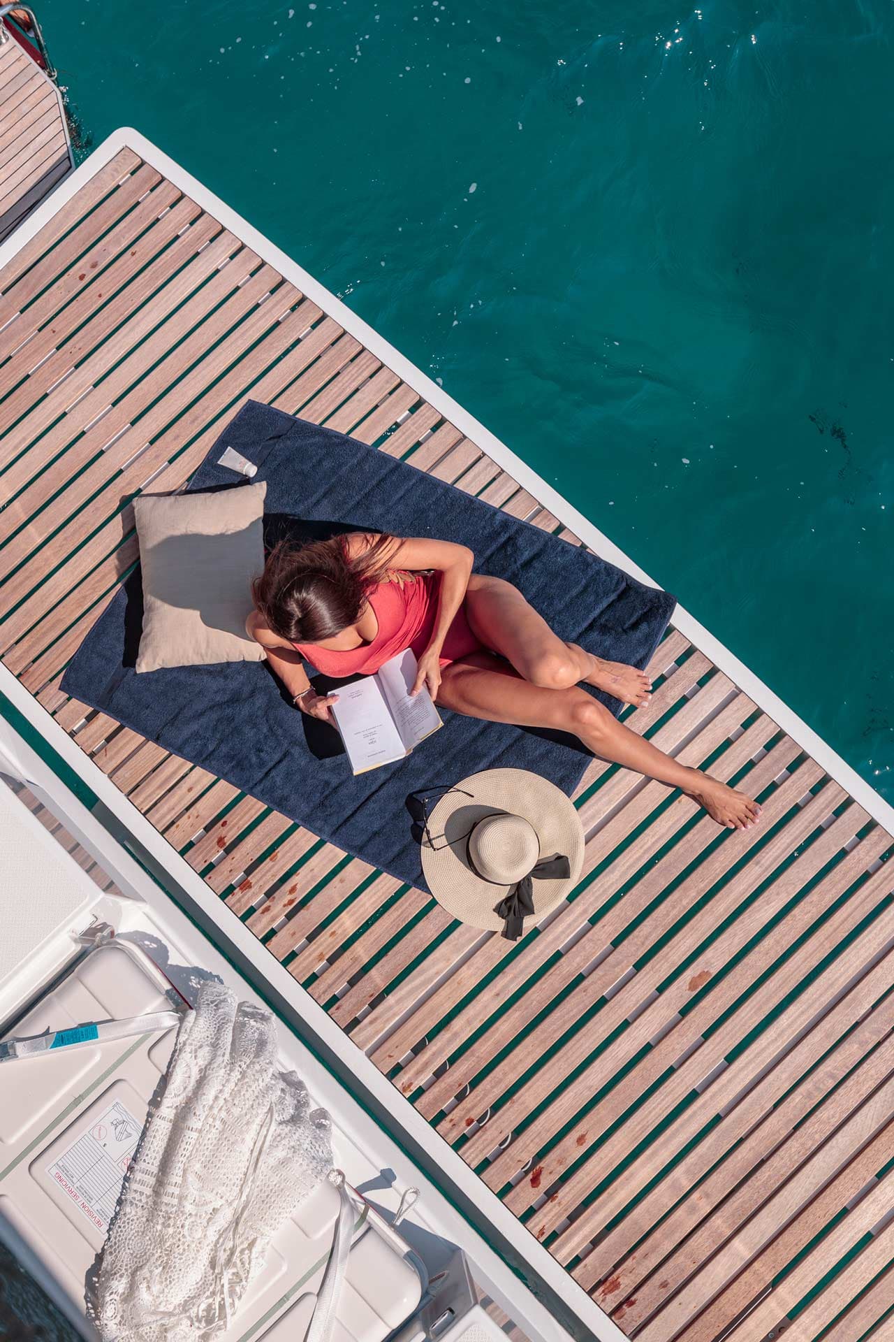 Kvinna i röd baddräkt läser en bok på en badbrygga.