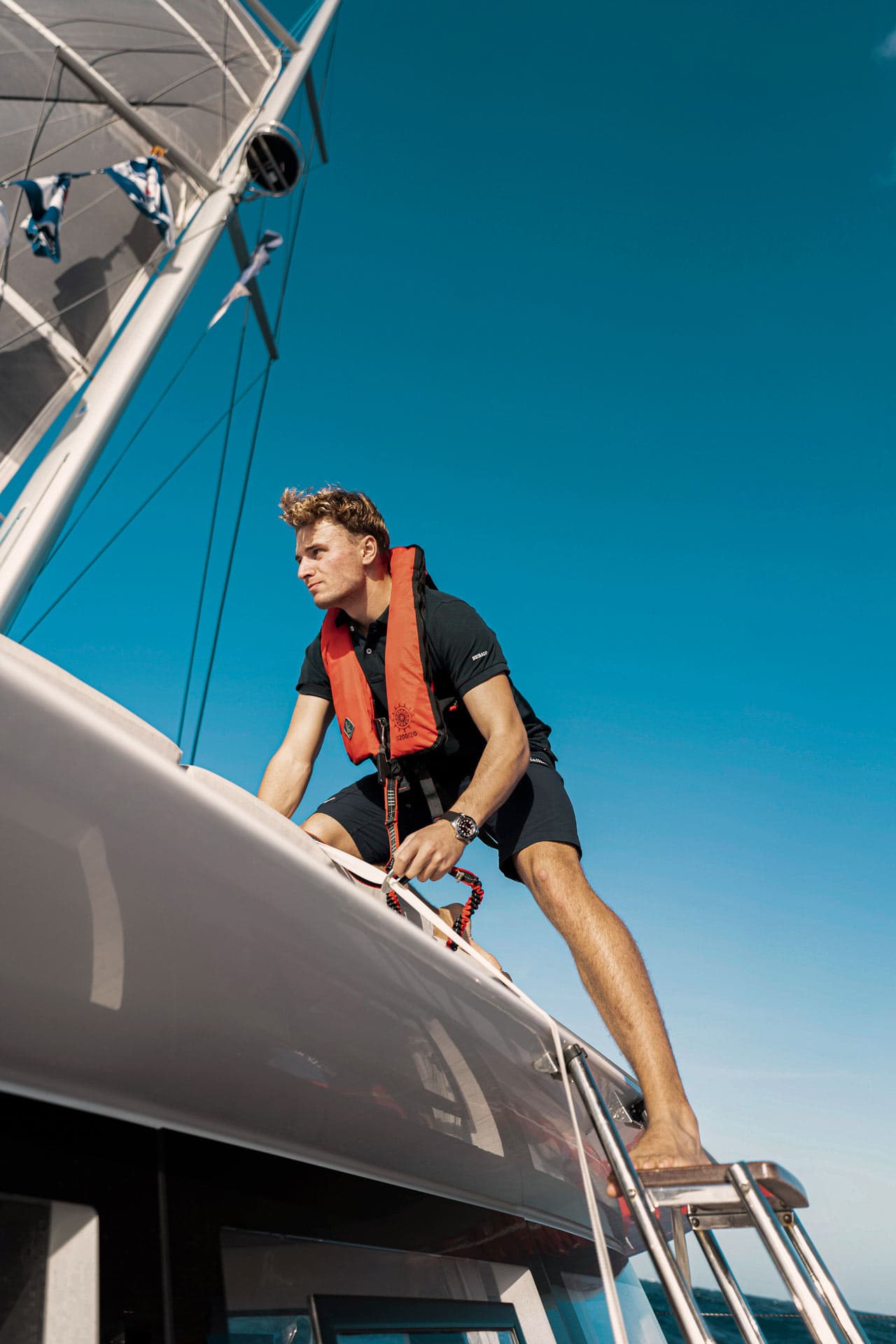Man standing ready on the roof of the catamaran with a safety rope in his hand