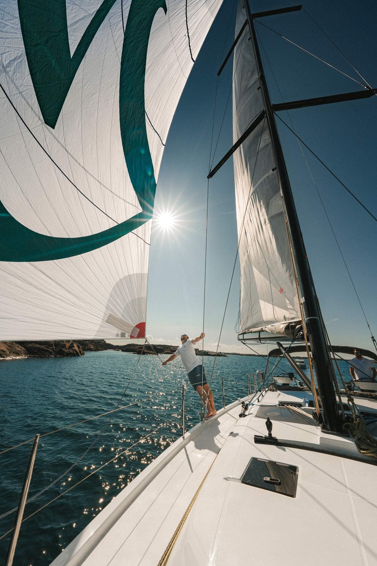 Eine Yacht unter vollen Segeln in der Sonne – ein Mann hält ein Segel vom Deck weg