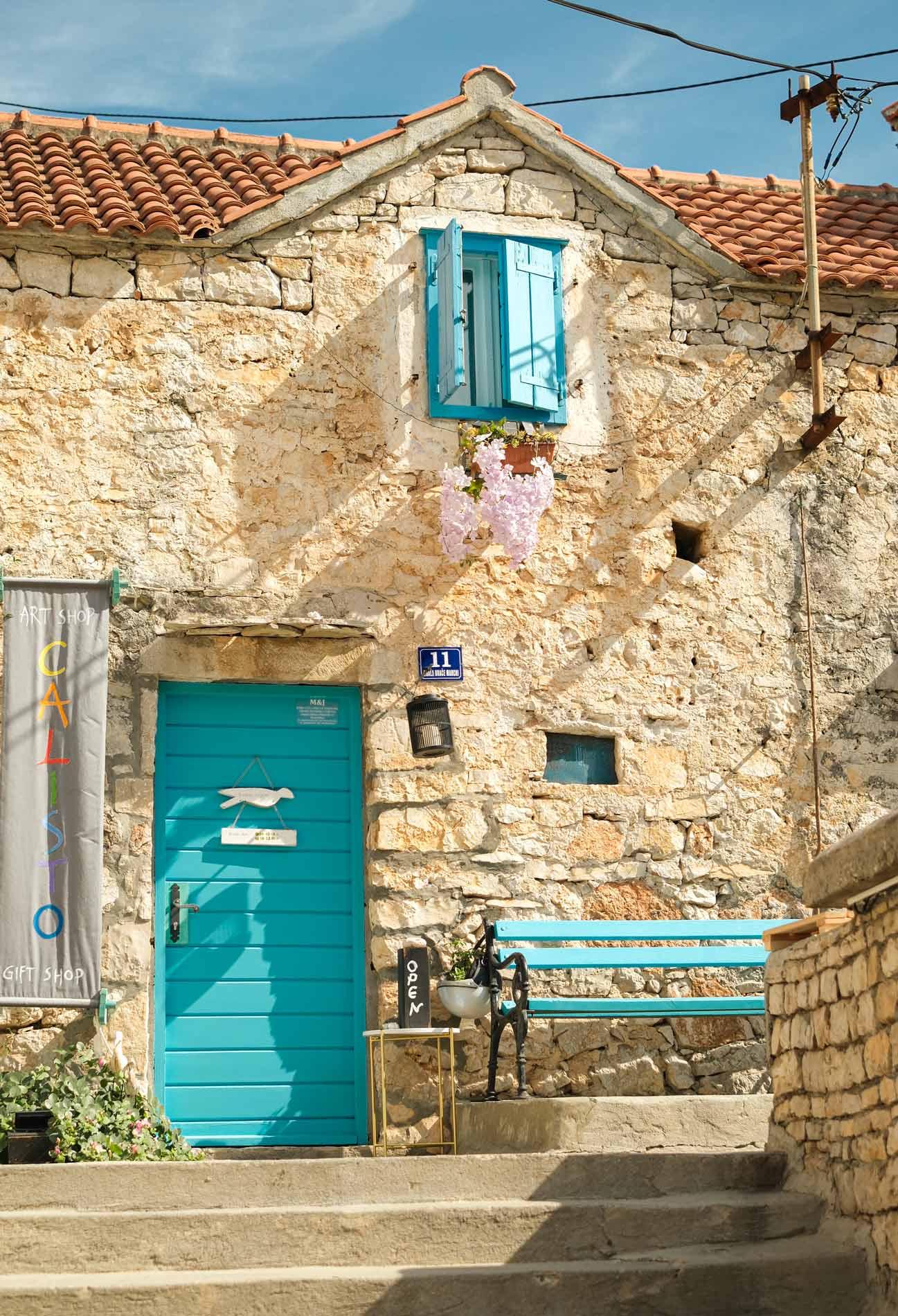 A cute stone house with a door, bench and shutters all in the same shade of blue