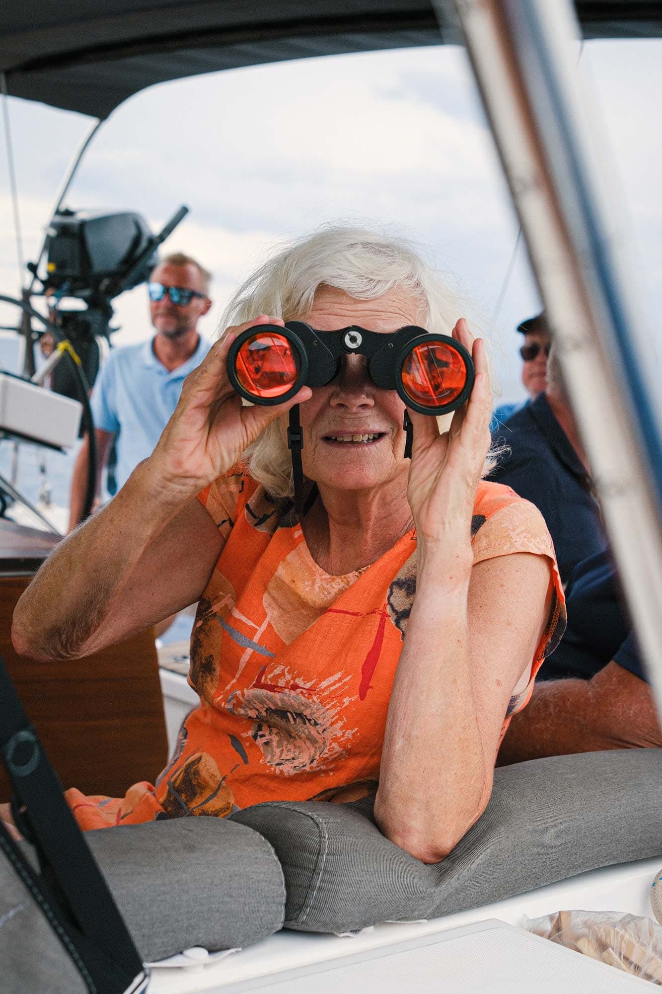 Eldre kvinne som ser ut mot havet med en kikkert.