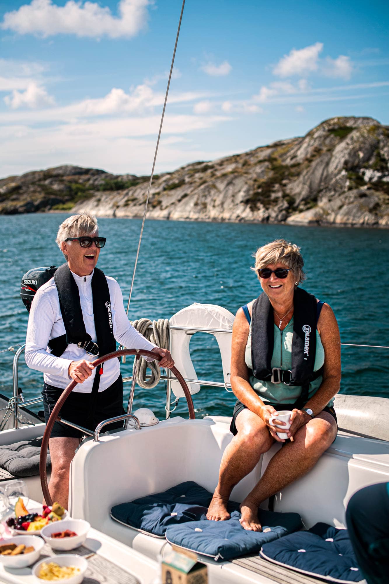 Zwei Frauen an Bord, eine steht am Steuer, die andere trinkt Kaffee