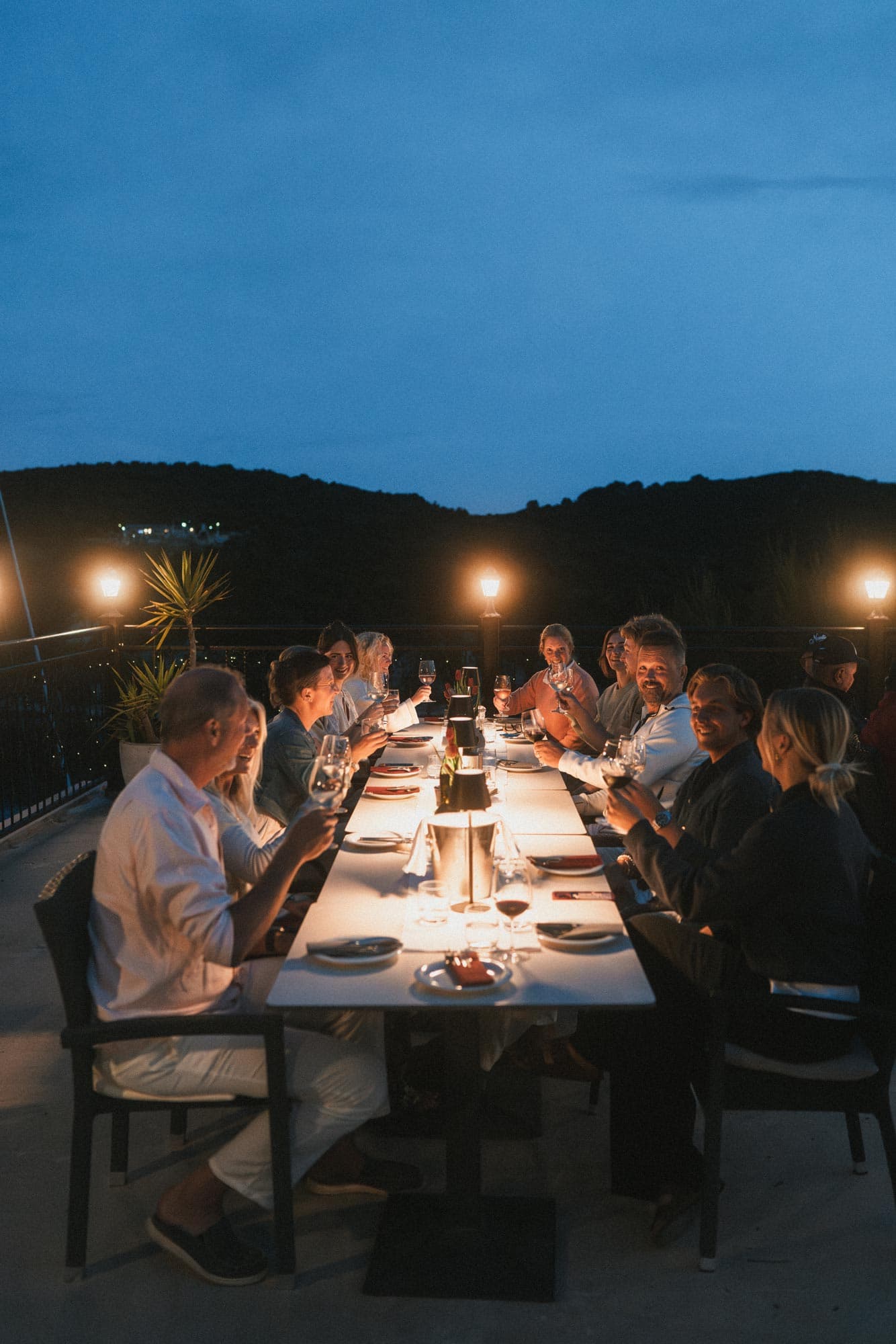 Twelve guests sit around a dinner table in a restaurant and make a toast