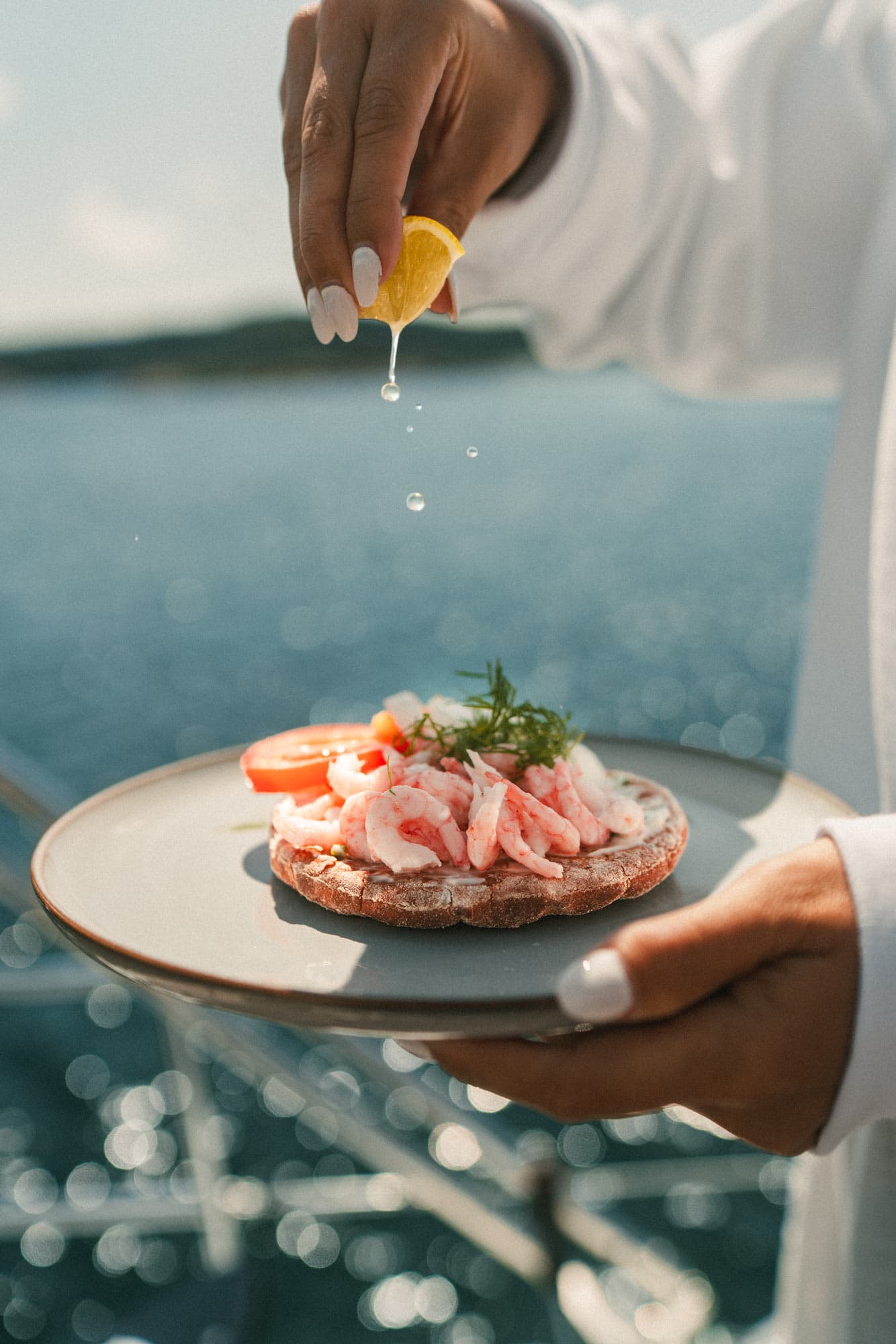 An open shrimp sandwich with tomato and dill. A lemon is squeezed over the top