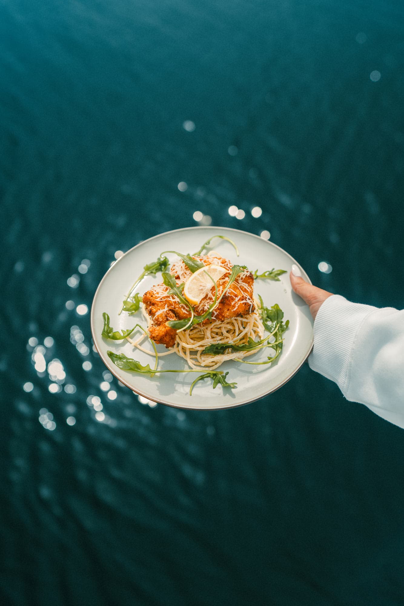 A plate with spaghetti, breaded chicken and rocket salad for lunch.