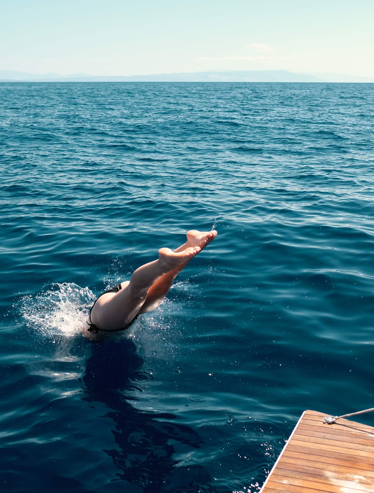A woman dives into the blue sea, with only her legs visible above the surface