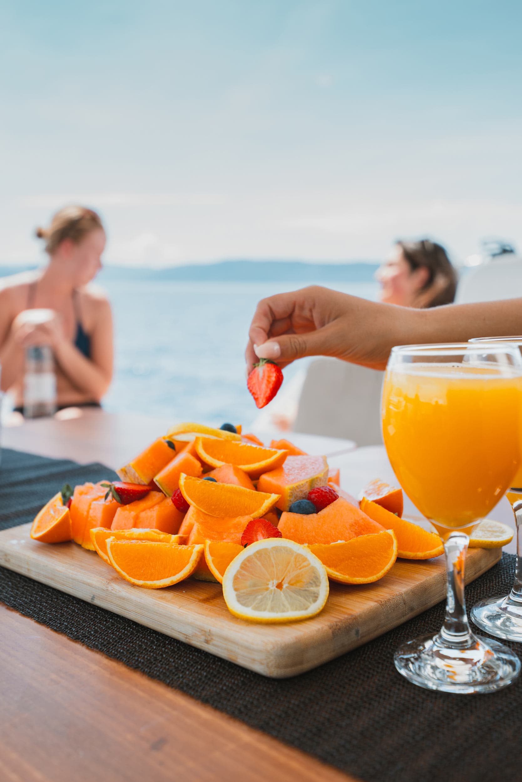 Deluxe fruit platter with orange, melon and strawberries. Two glasses of juice to the side.