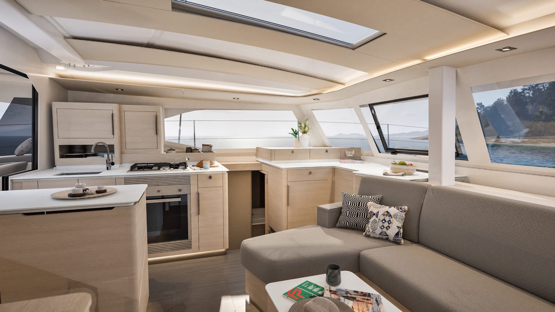 Bright lounge on board a catamaran with sofa and cushions, wooden cupboards and a white worktop. 