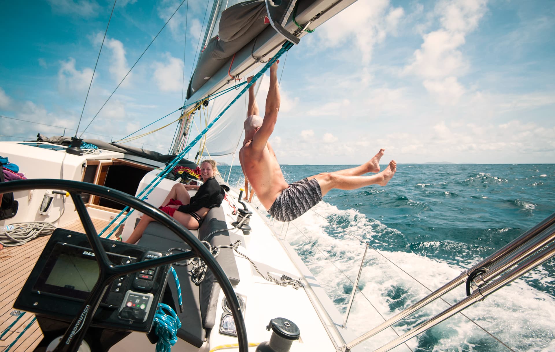 A man holding onto the mast while swinging his legs out when sailing