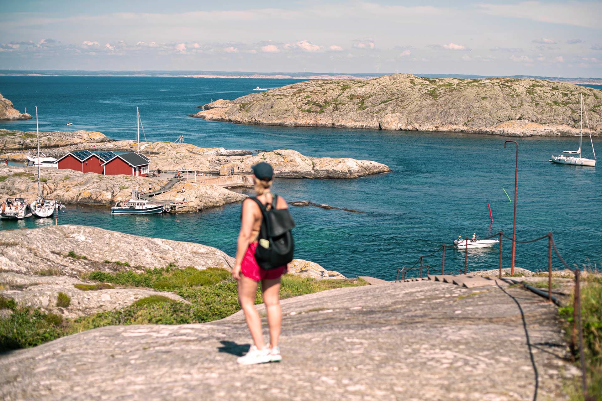 A woman stands on a boulder and looks out over the harbour entrance towards Väderöarna