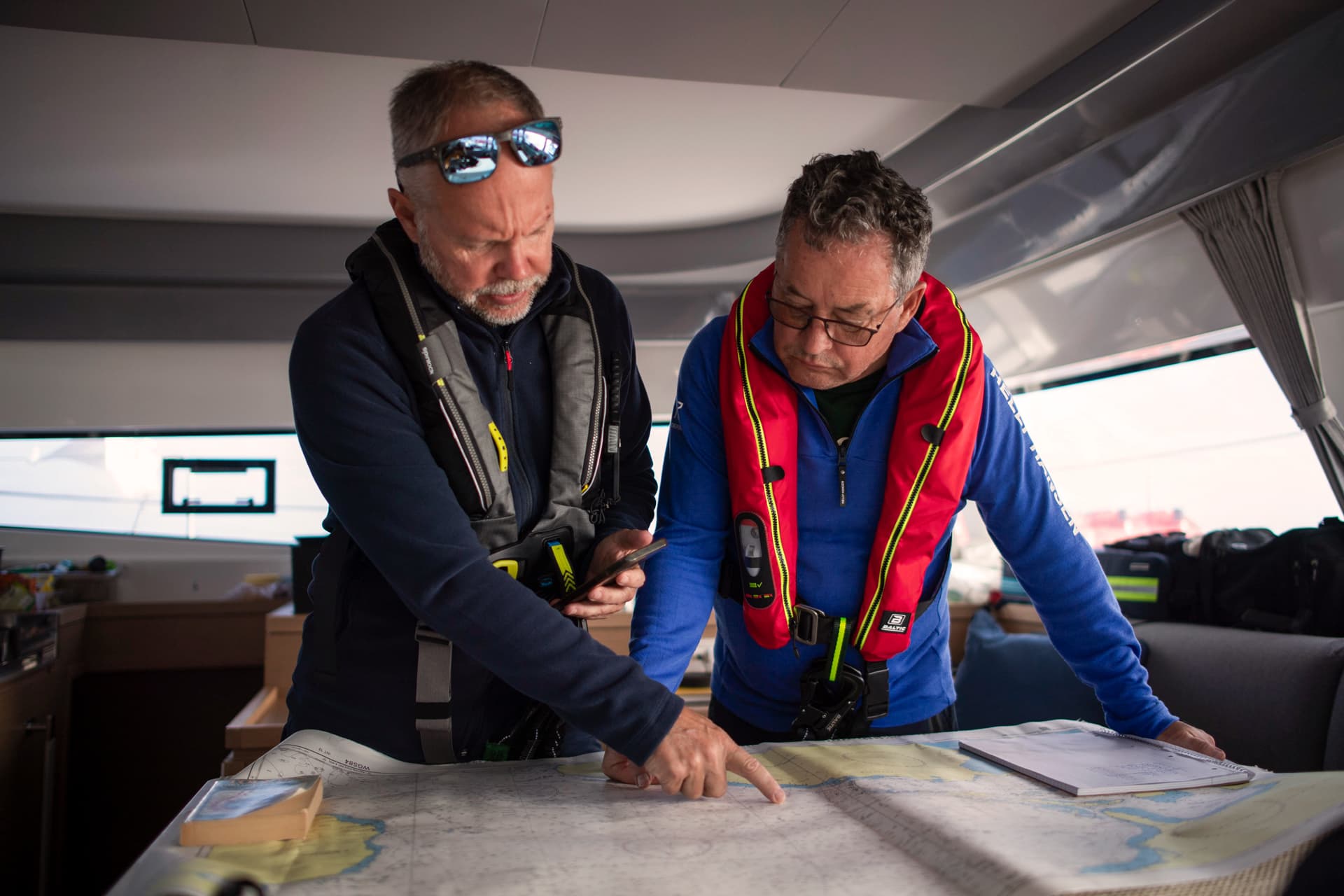 Zwei Männer in Schwimmwesten betrachten eine Seekarte und planen eine Route