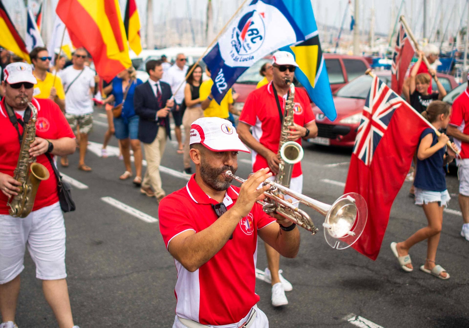 People walk in a parade wearing red tops and playing wind instruments.