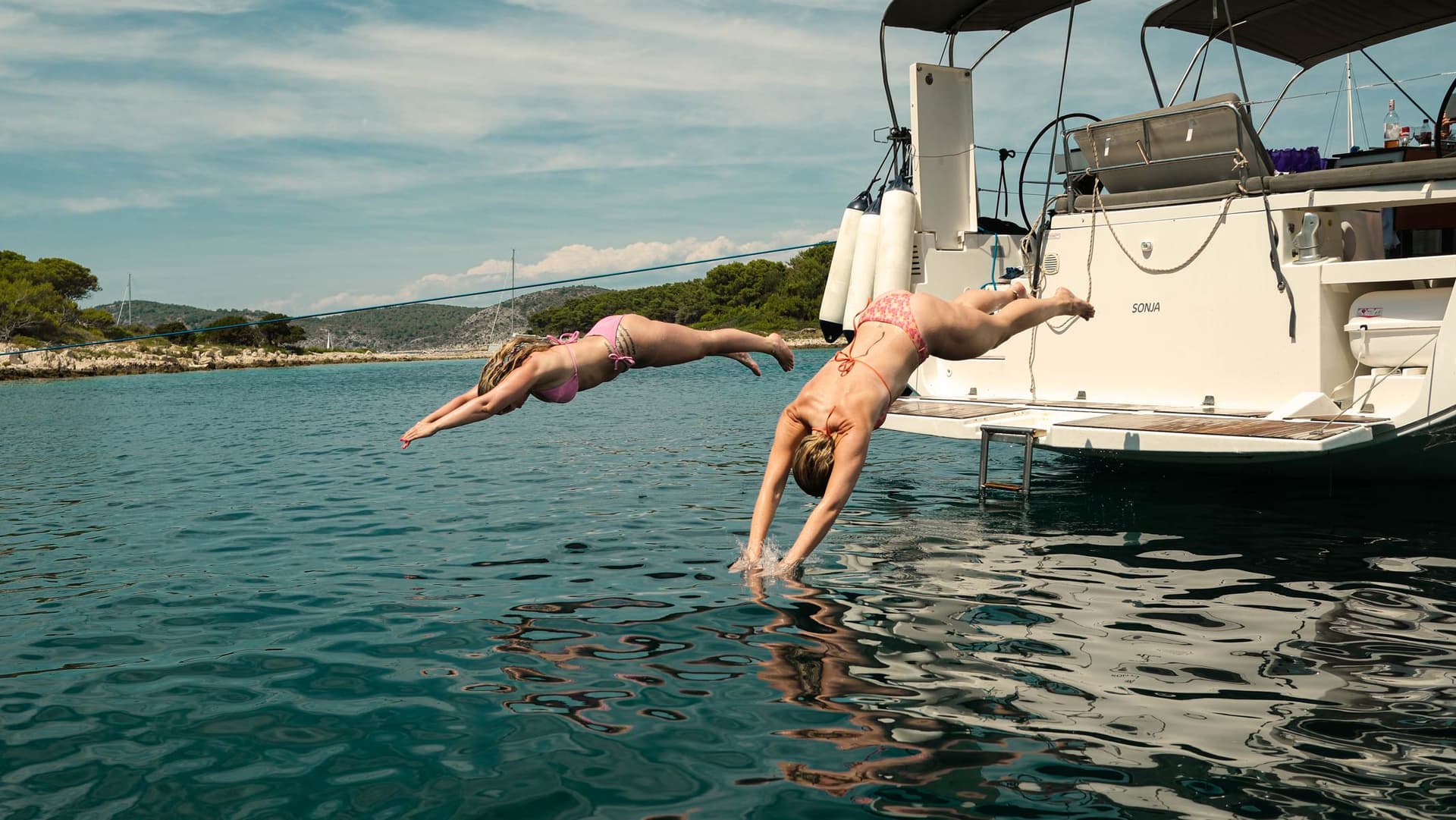 Zwei Frauen springen im Kopfsprung von der Badeplattform ins Wasser