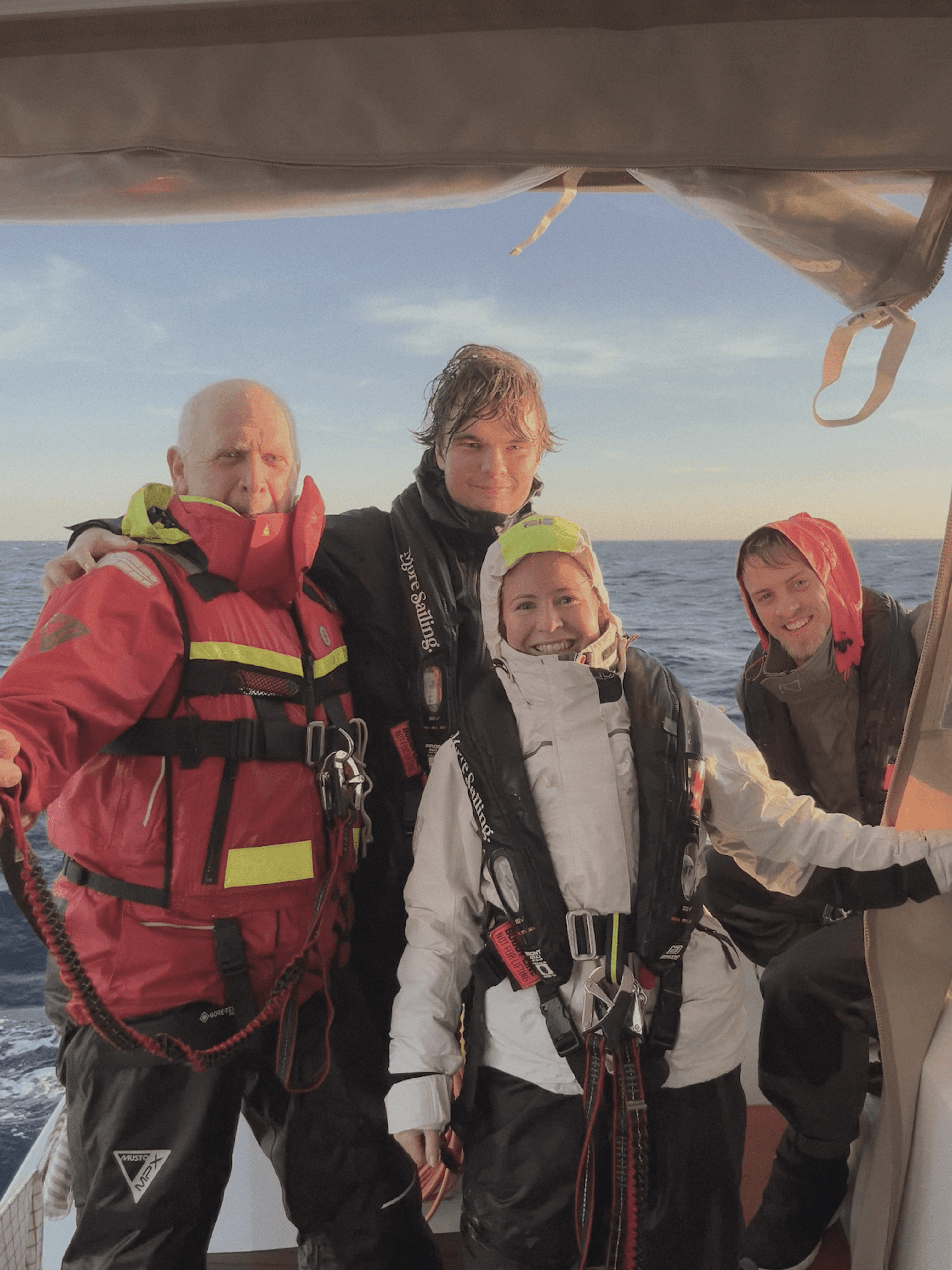 Tre män med flytvästar och solglasögon betraktar segelsättningen ombord på en segelbåt.