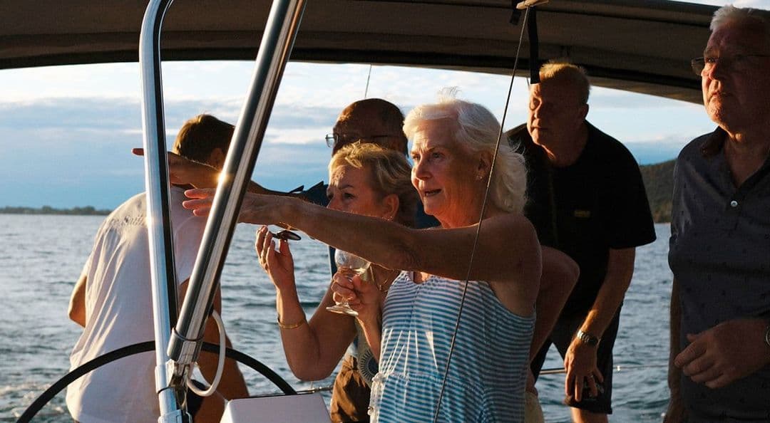 En grupp äldre människor tittar ut mot havet. En kvinna pekar.