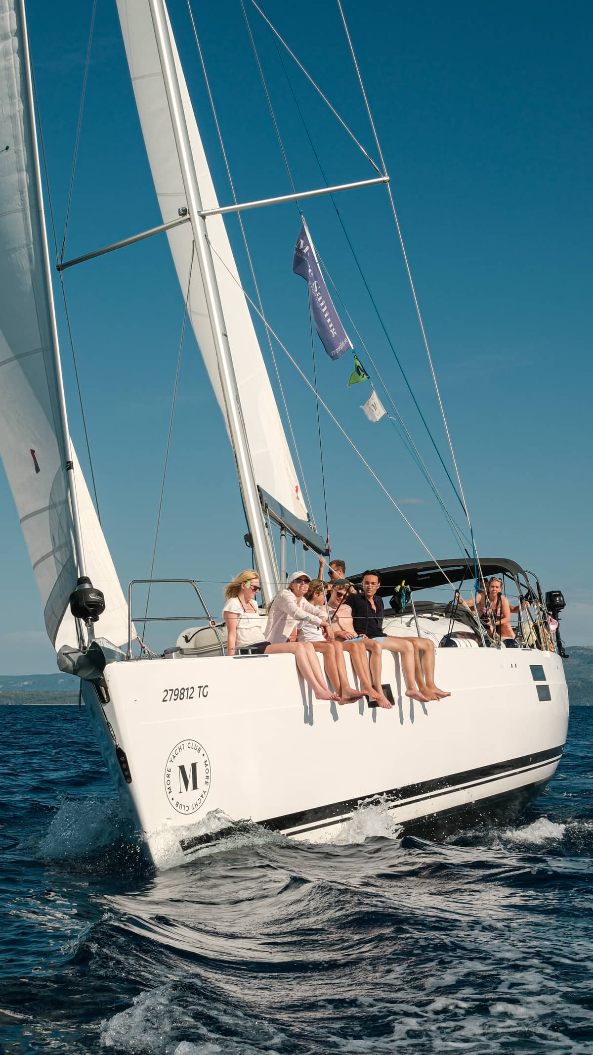 Segelndes Boot, auf dem eine Gruppe sitzt und mit den Beinen über der Bordkante baumelt