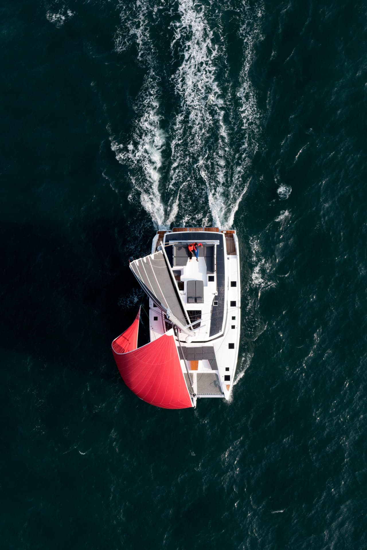 Seglande katamaran med rött segel.