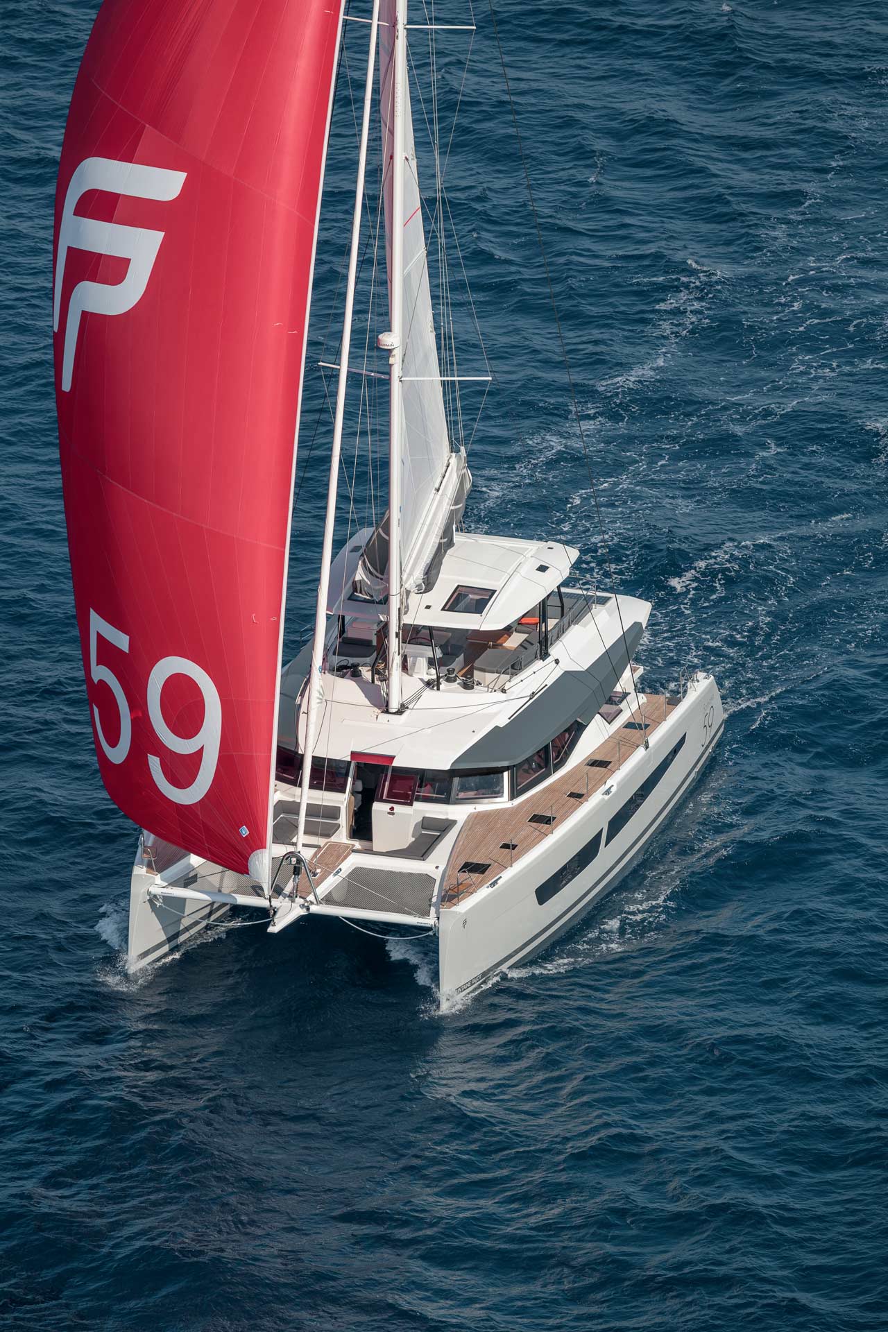 Vit katamaran med rött segel seglar på havet.
