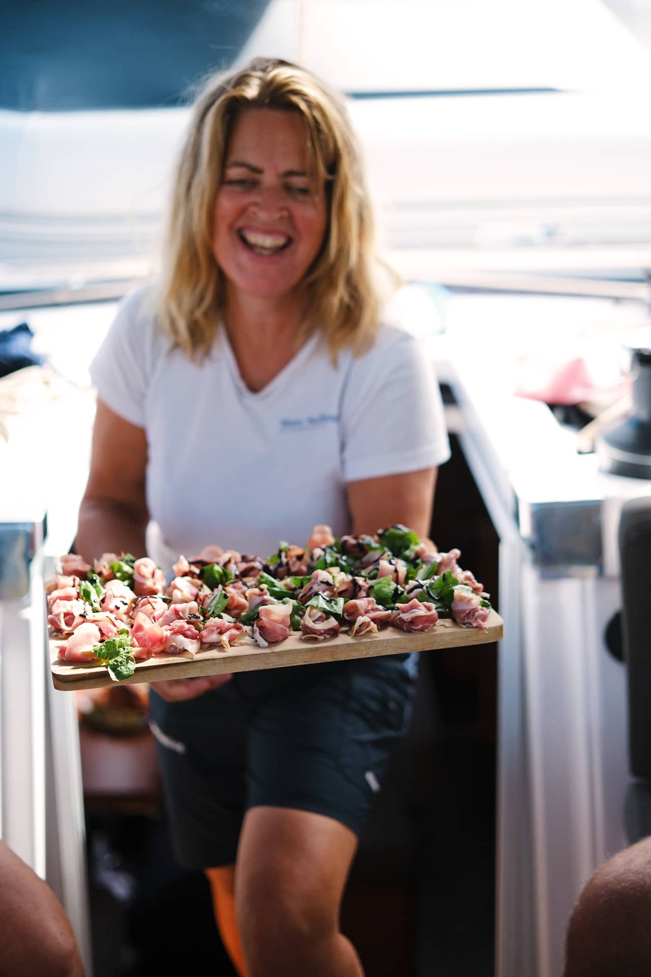 Der Gastgeber kommt aus dem Boot an Deck mit einem Tablett mit luftgetrocknetem Schinken, grünem Salat und Balsamico-Essig