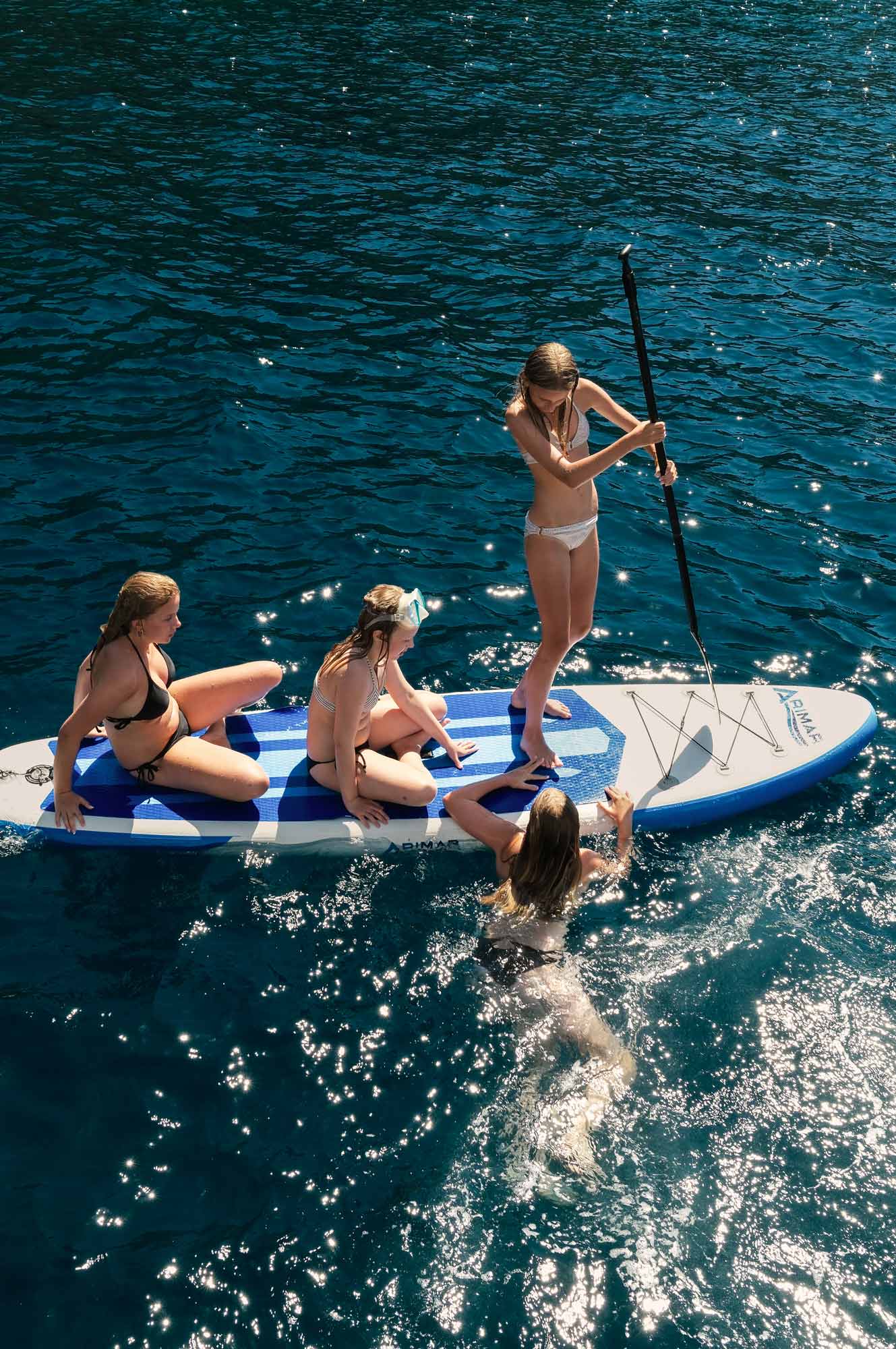 Four children playing in the water with a stand up paddle board