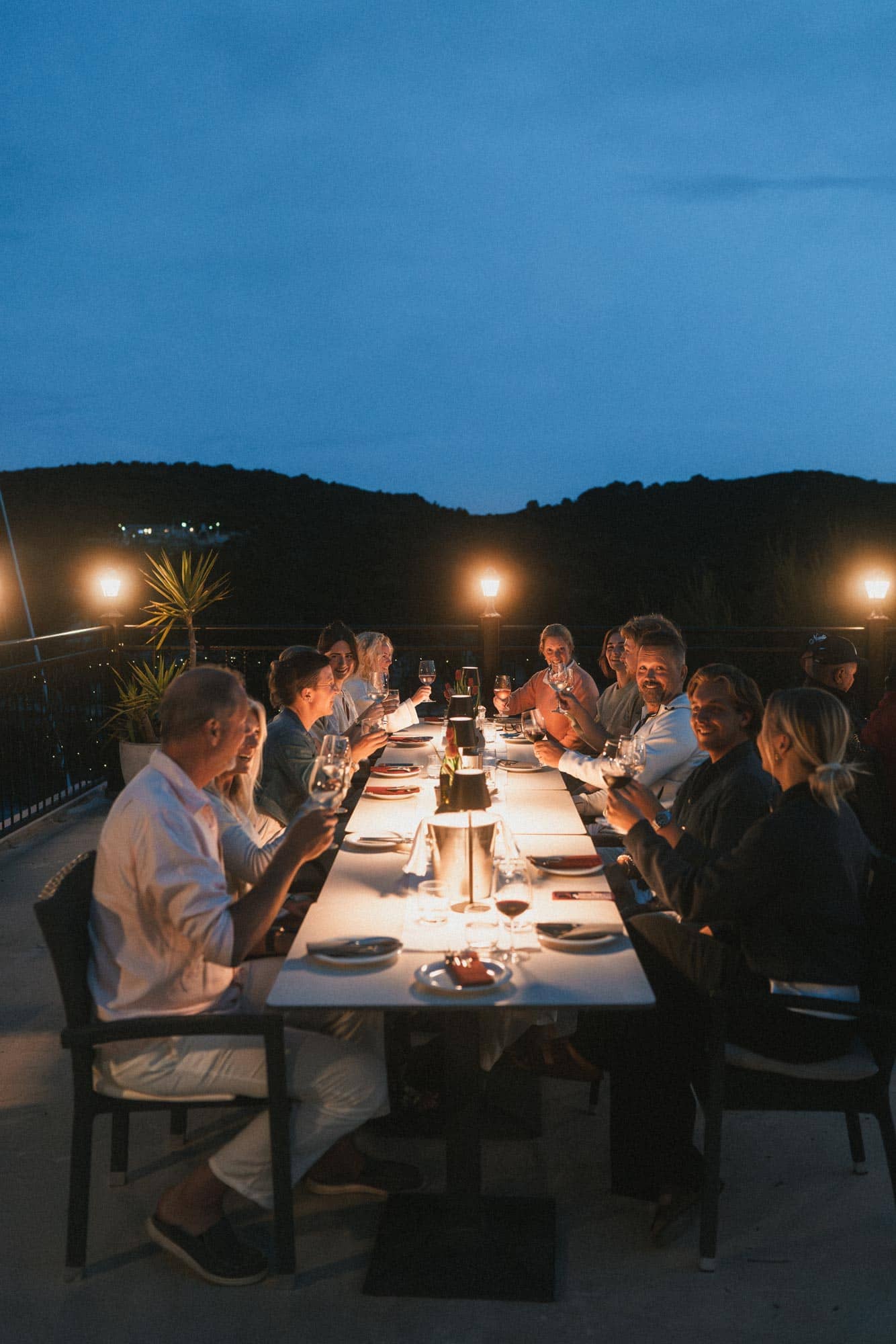 Twelve guests sit around a dinner table in a restaurant and make a toast