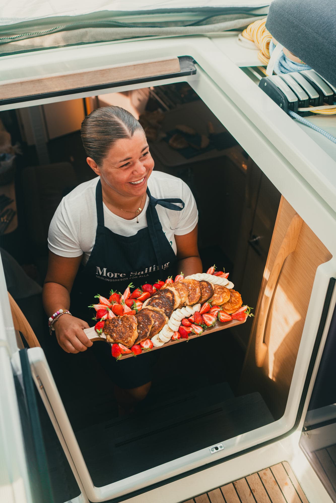 Ein Gastgeber kommt die Treppe hinauf mit einem Tablett mit kleinen Pfannkuchen, Erdbeeren und Bananenscheiben.