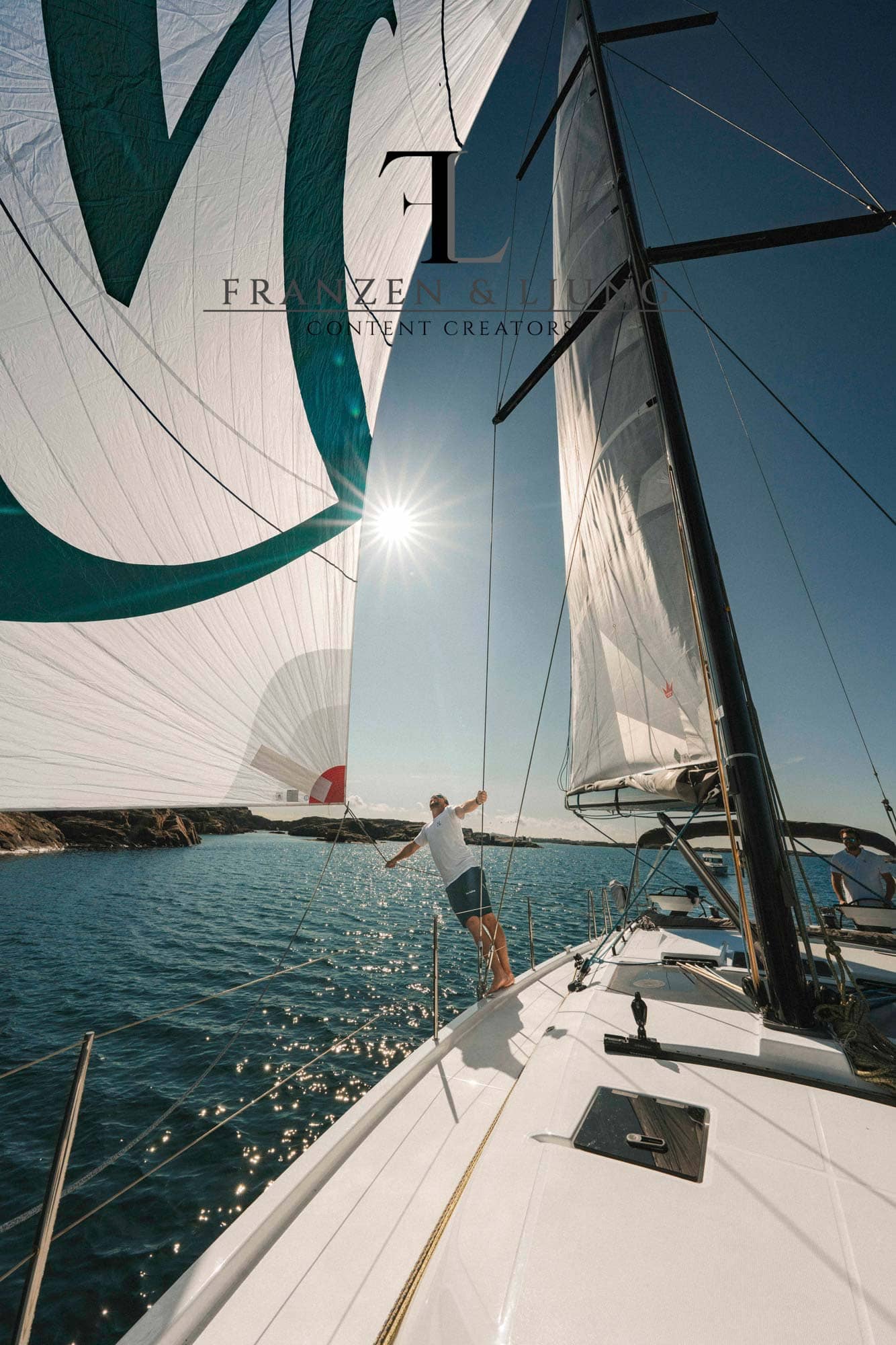 Eine Yacht unter vollen Segeln in der Sonne, ein Mann hält ein Segel vom Deck weg