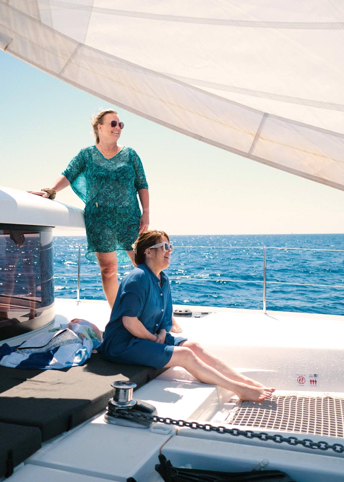 Two women standing on the foredeck of a catamaran, reading