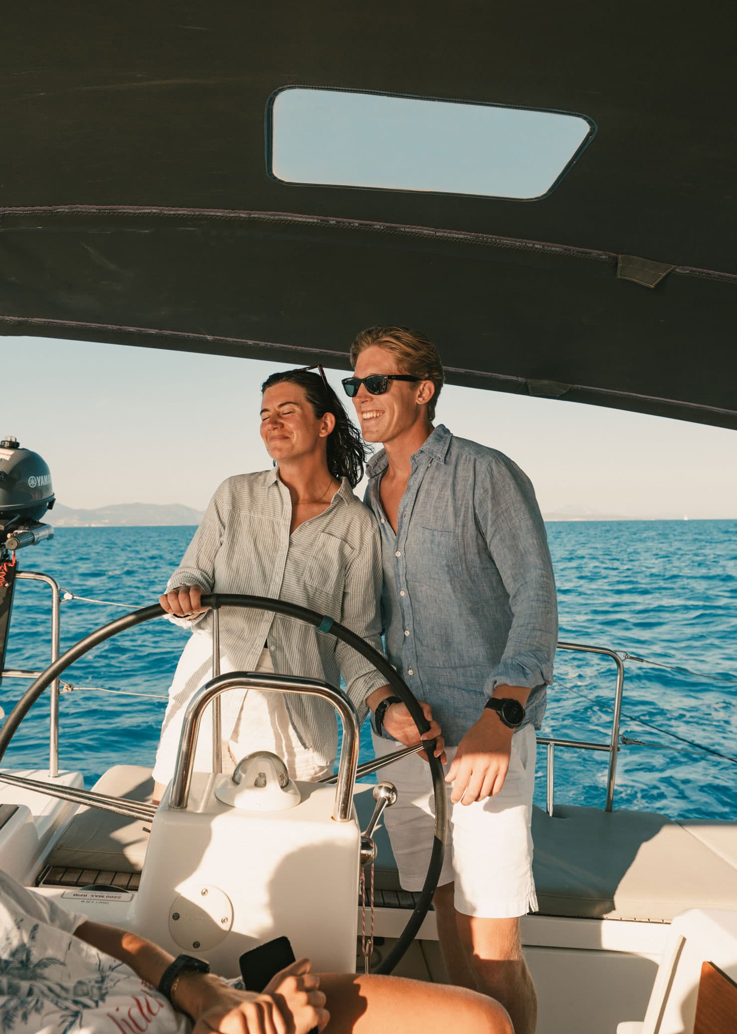 A couple taking the helm of a sailboat.