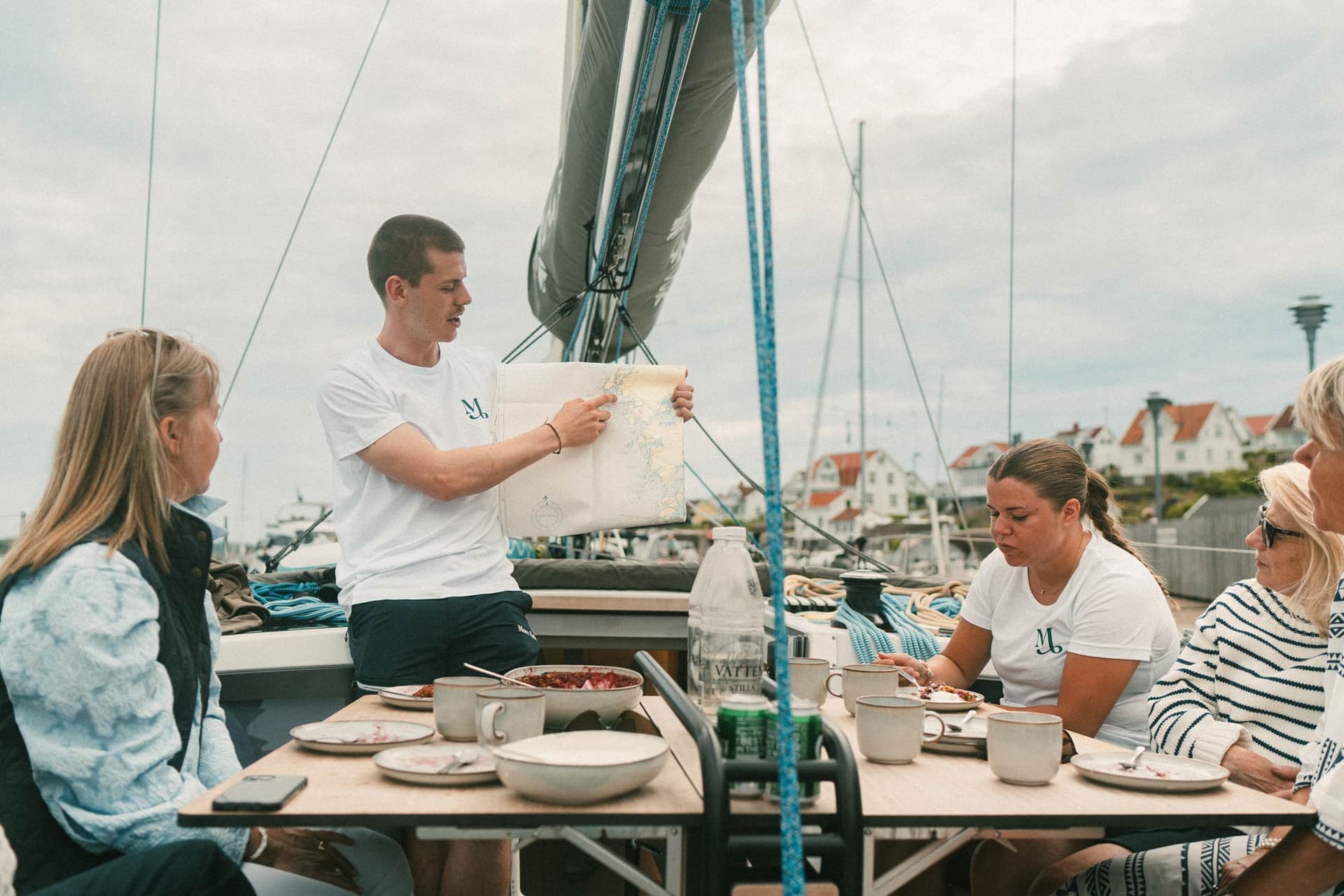 En skeppare visar på en karta vilken rutt båten ska ta. Gäster tittar på.