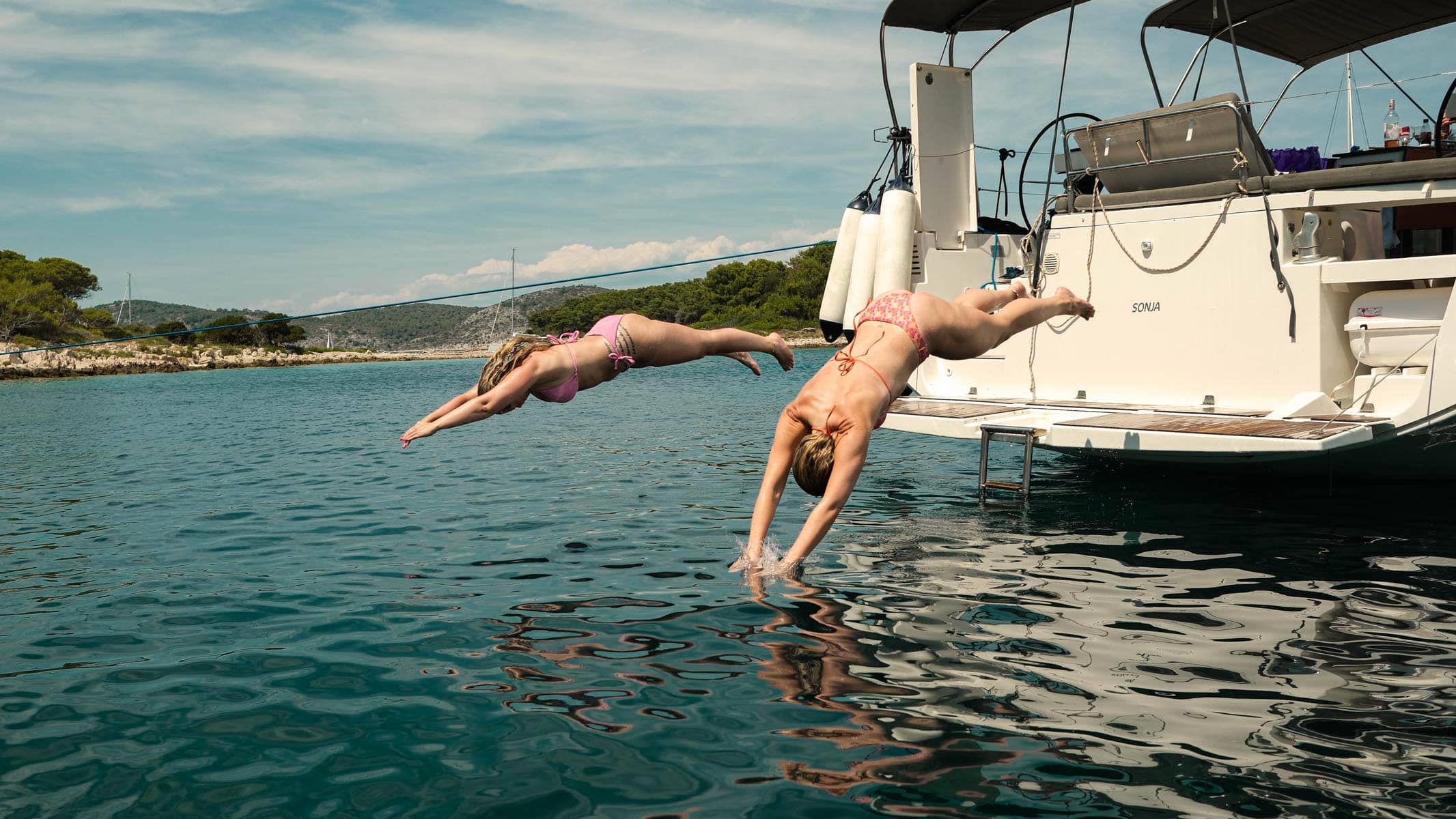 Två kvinnor som dyker ner i vattnet från badbryggan