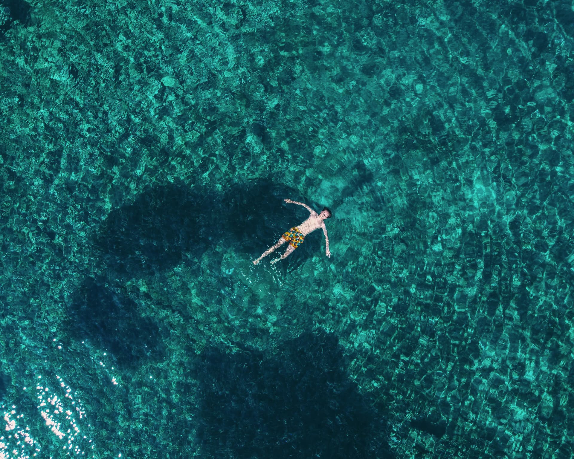 Mann schwimmt im türkisfarbenen Wasser auf dem Rücken.