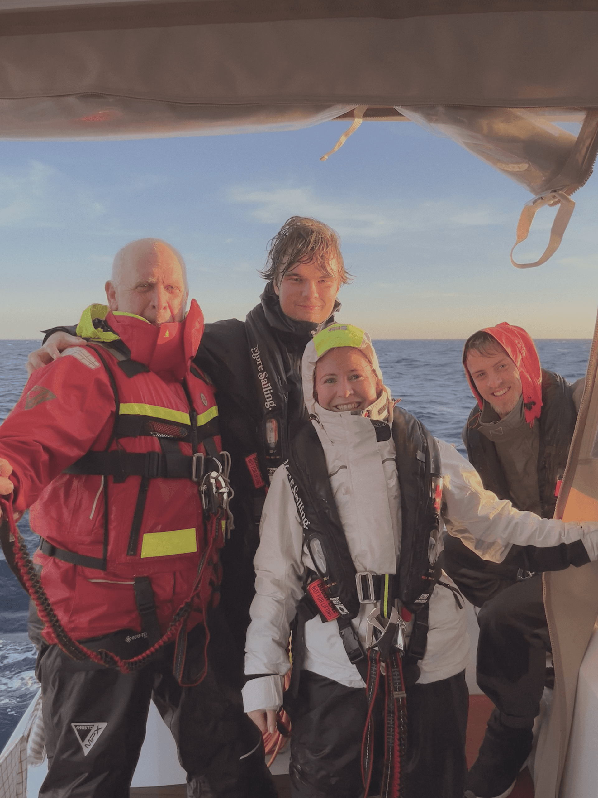 Tre män med flytvästar och solglasögon betraktar segelsättningen ombord på en segelbåt.